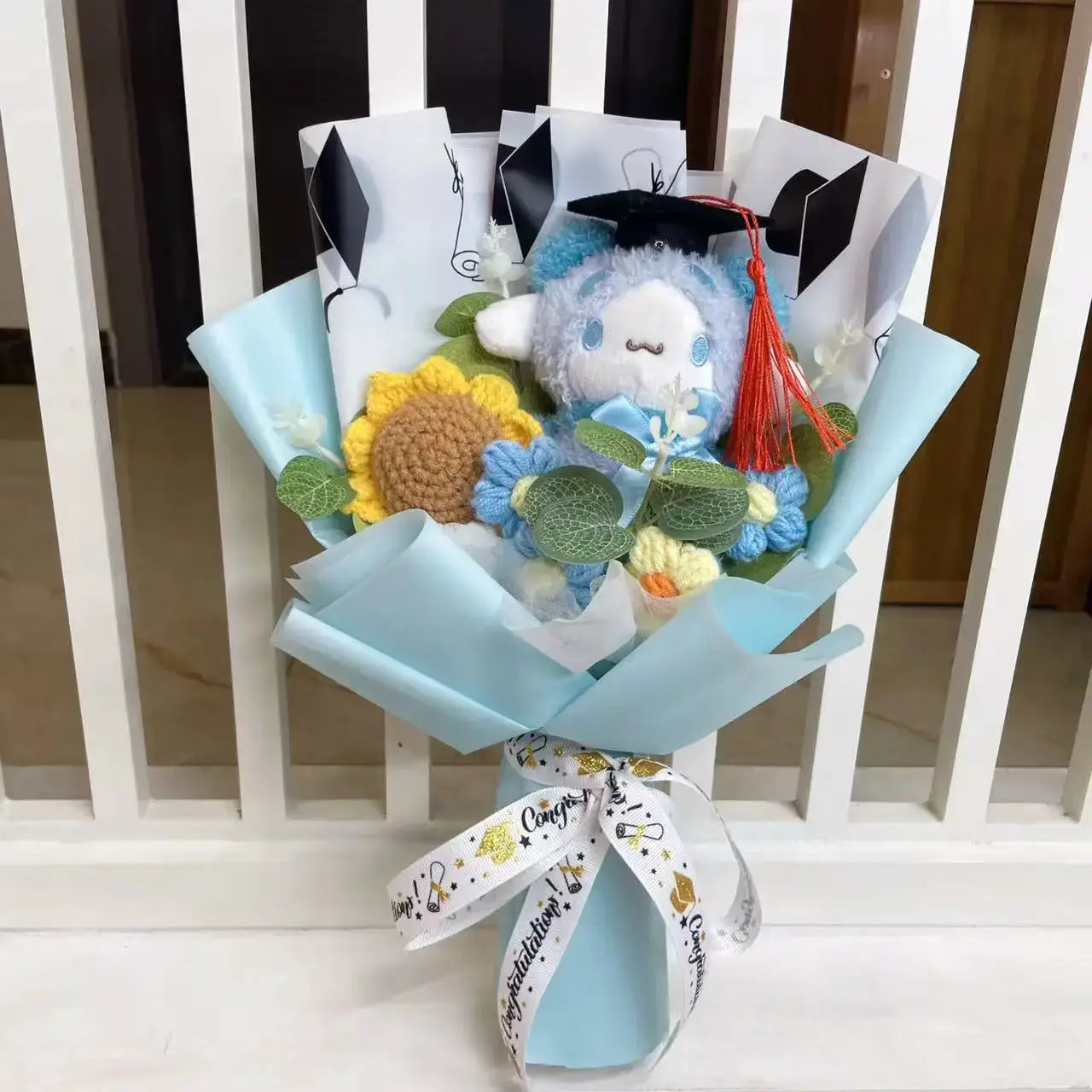 Stuffed plant bouquet by Simples Market: blue plush with grad cap, sunflowers, and crocheted blooms in pale blue wrap.
