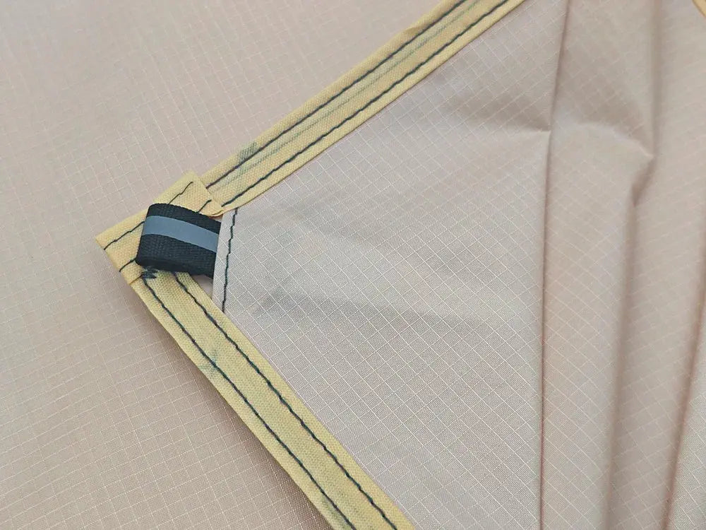 Waterproof camping mat by Simples Market with beige fabric and yellow carry strap, peg loops.