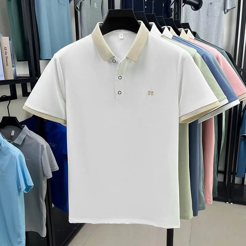White polo shirt with beige collar and cuffs, small embroidered chest logo; multiple pastel polos on rack behind.