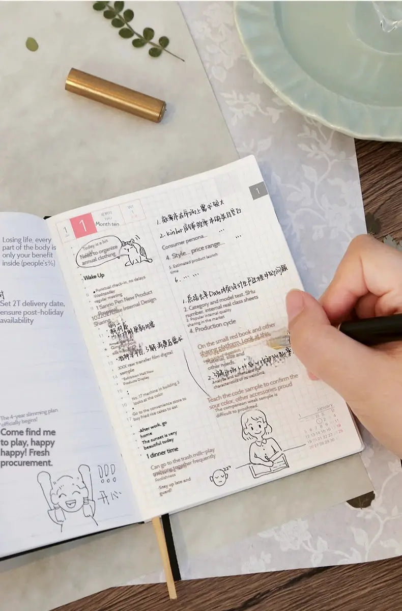 Kinbor Notebook 2026 planner, white grid pages, A5/A6 size, open on desk with hand writing.