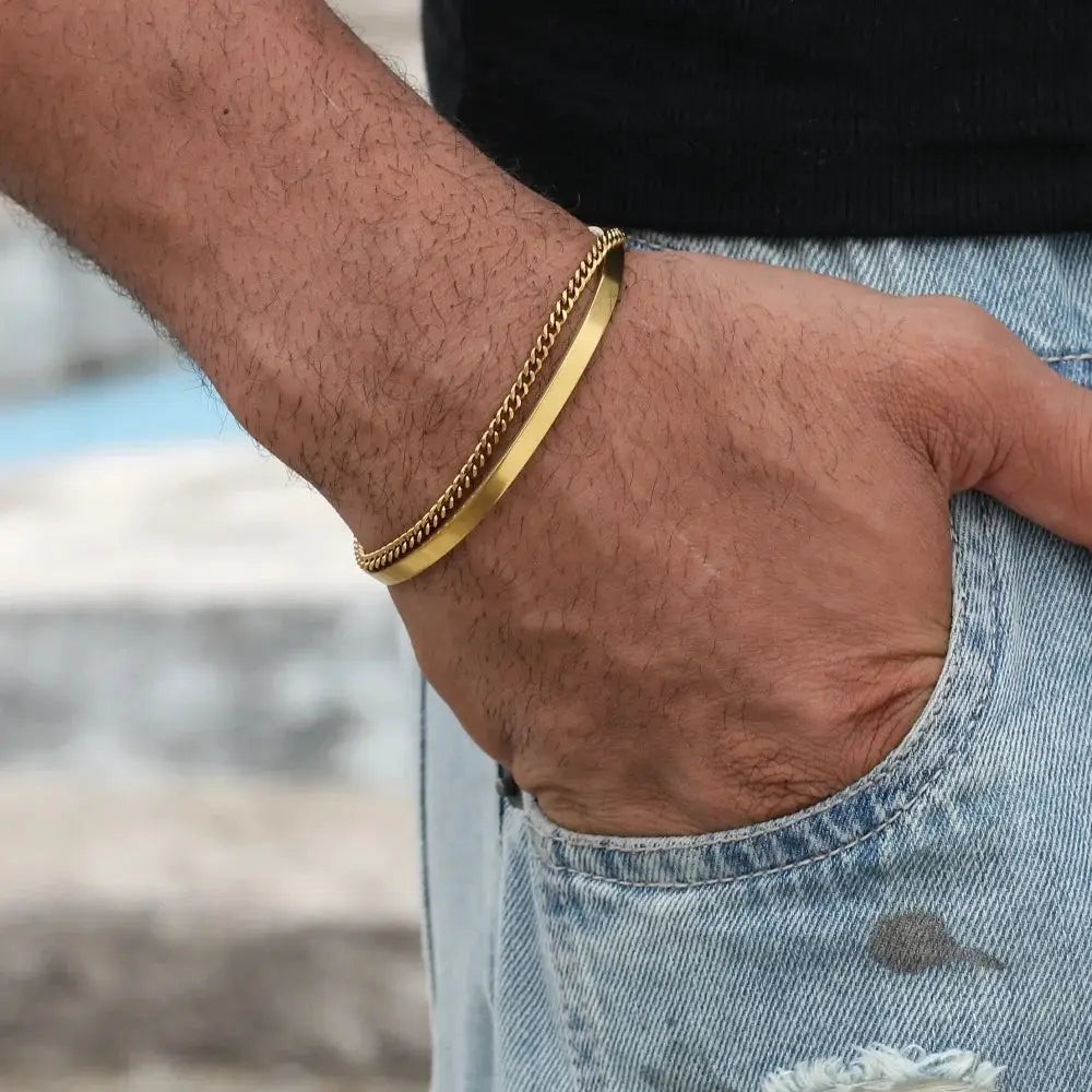 Two gold-tone bracelets on a man's wrist: a 3mm stainless steel Cuban chain bracelet with adjustable open design and a second gold-tone chain bracelet.