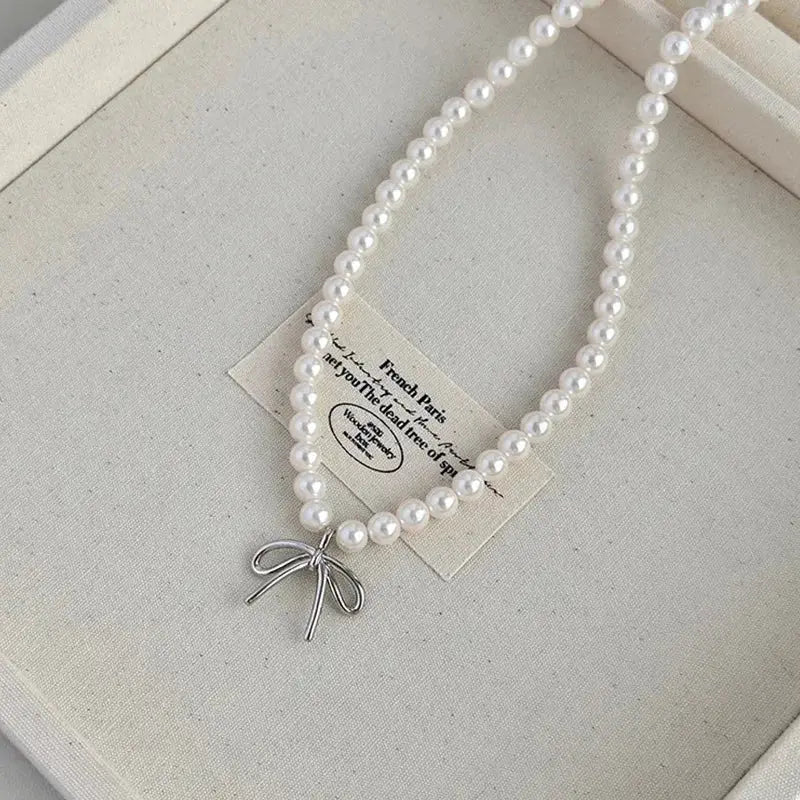 Imitation pearl necklace, white collarbone-length choker with a silver bow pendant