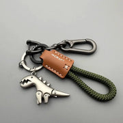 Motorcycle and car keychain with metal T-Rex dinosaur charm, green braided rope, brown leather tag with white stitching, and metal carabiner clip