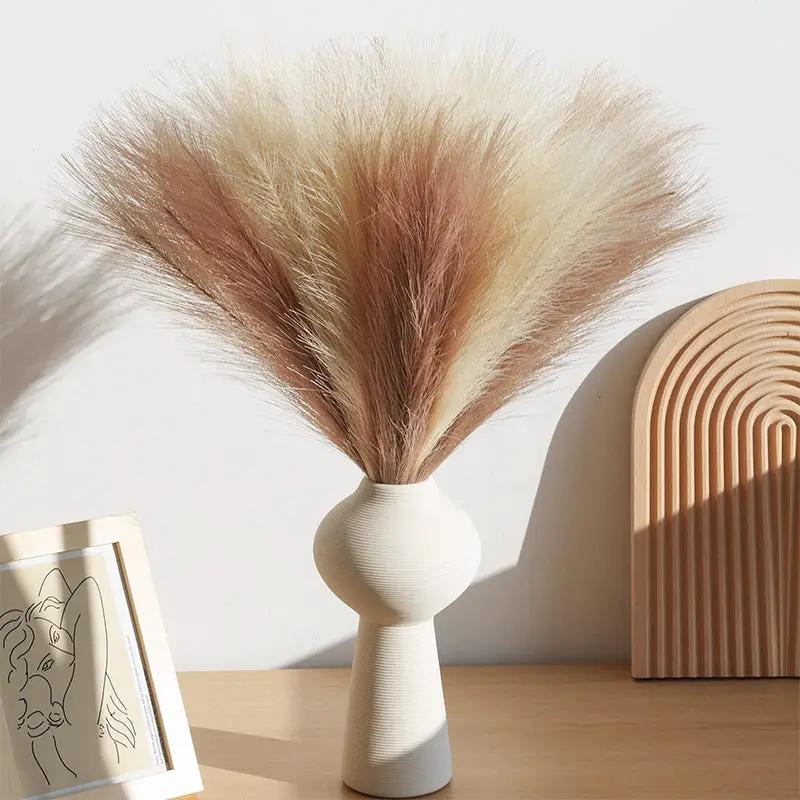 Artificial pampas grass bouquet in beige-brown plumes in a white ceramic vase, boho decor.