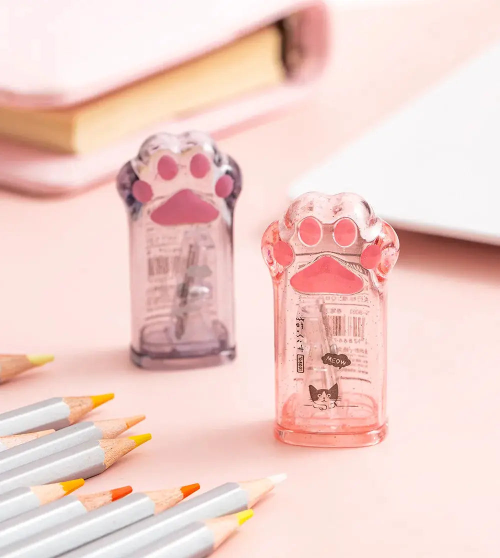Two kawaii cat-paw shaped pencil sharpeners in pink and purple translucent plastic.
