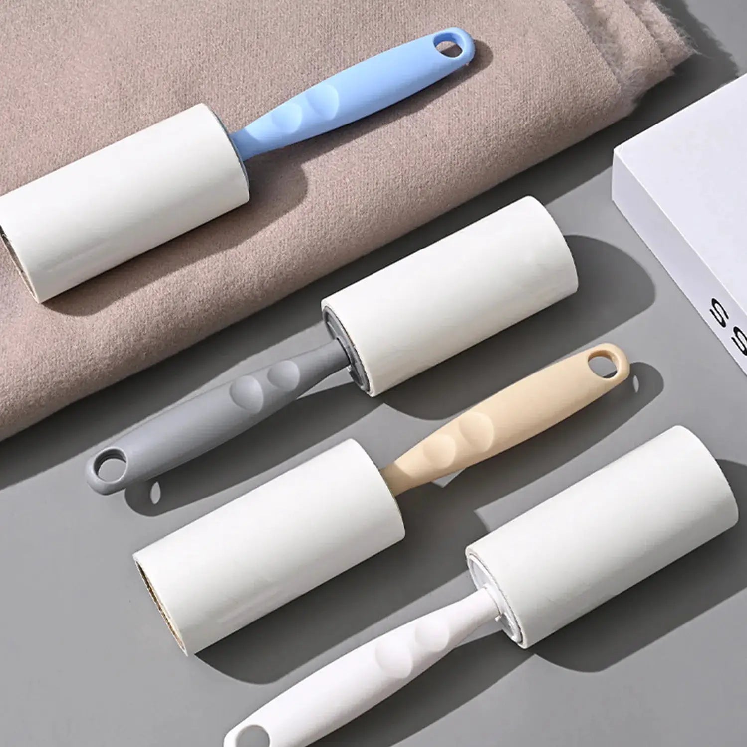 Lint roller set with replaceable rolls and pastel-colored handles blue gray beige