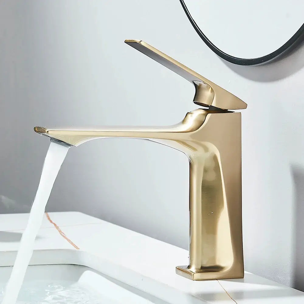 Deck-mounted bathroom faucet by Simples Market in brushed gold with single lever, water flowing into sink.