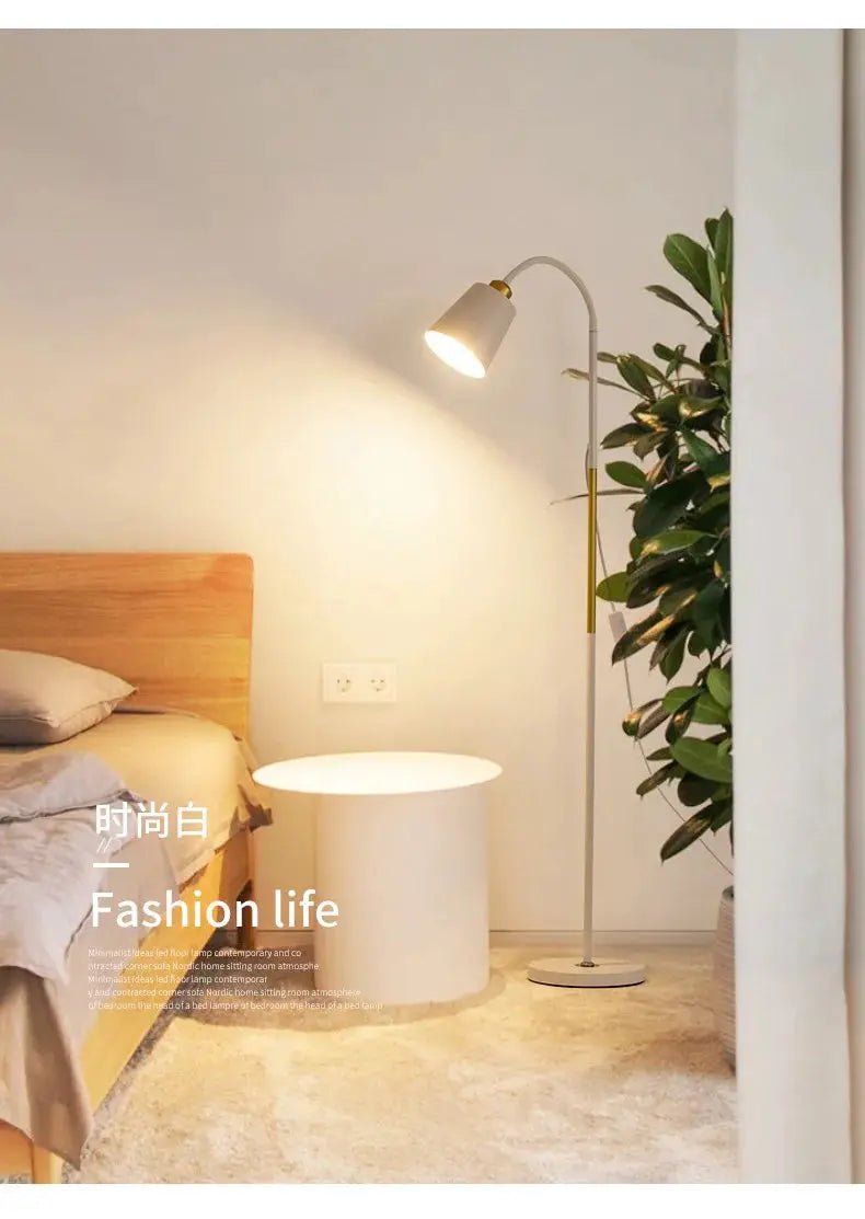Floor lamp Simples Market; white adjustable LED standing lamp with brass accents in a cozy bedroom beside bed and plant.