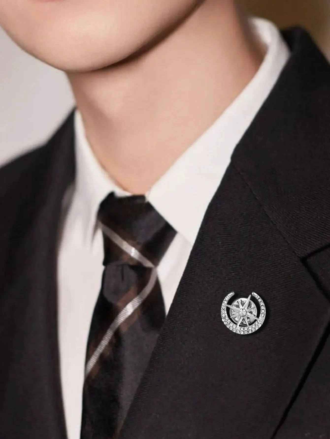 Silver-toned crystal lapel brooch with circular design worn on a black suit jacket