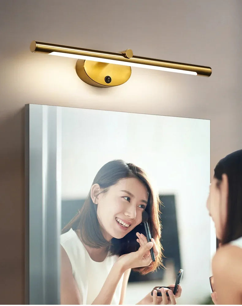 Modern LED wall lamp in brass finish with touch switch mounted above a bathroom mirror.