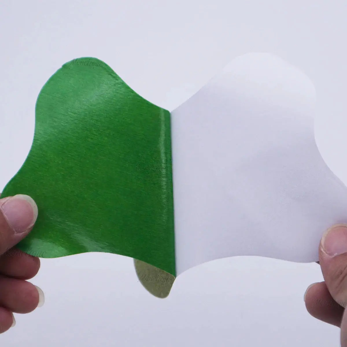 Lumbar self-heating patch with green adhesive side peeling from white backing