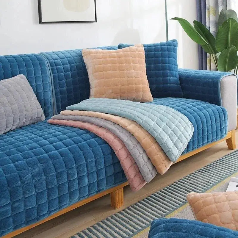 Velvet sofa cover by Simples Market; blue quilted cover with matching cushions and pastel throws on a wooden sofa.