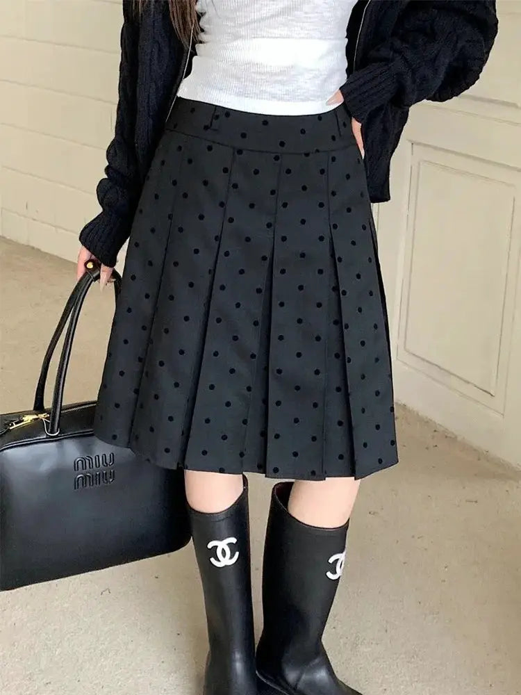 Polka dot pleated high-waist black skirt; A-line silhouette with dots, styled with Chanel boots.