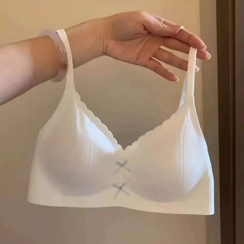 Women's white wireless sports bra with gathered cups, scalloped neckline, thin straps, and front bow accents