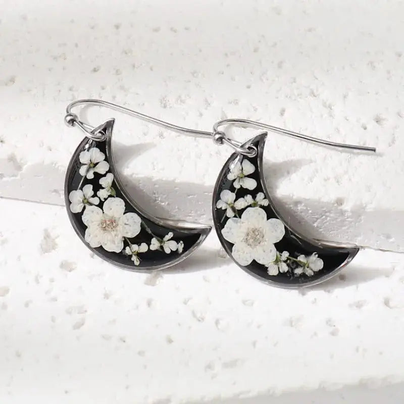 Moon crescent earrings with pressed white flowers in black epoxy resin; silver hooks, pair.