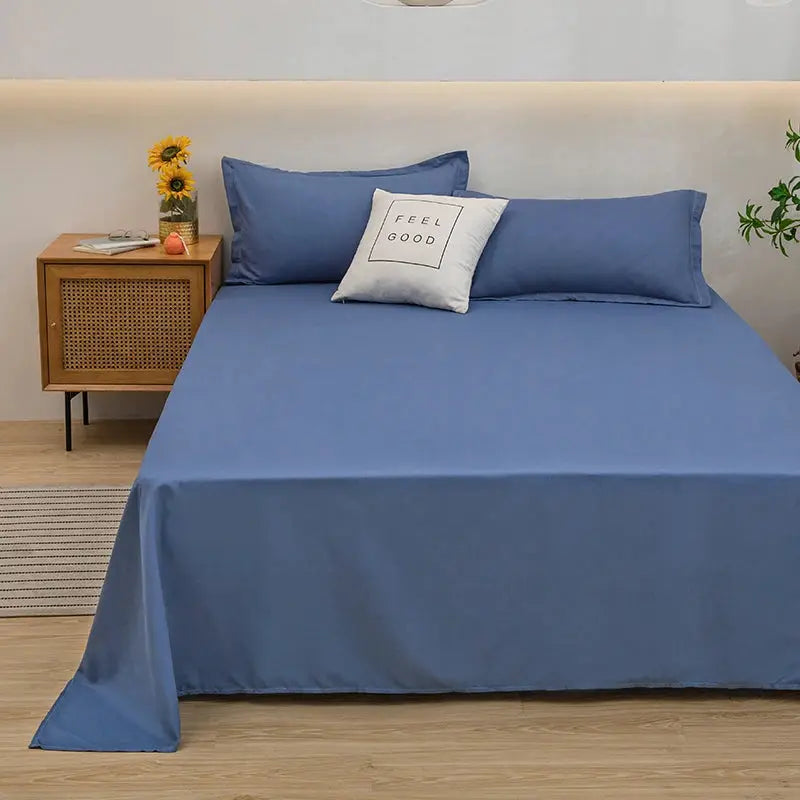 Blue bed flat sheet for double bed with matching blue pillowcases and a white decorative cushion.