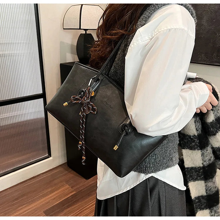 PU leather shoulder bag by Simples Market, black with rope-tie tassel, worn as a crossbody.