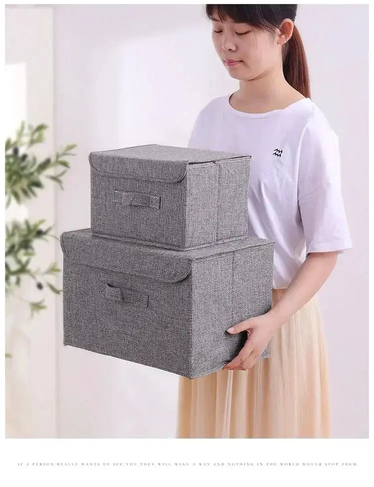 Grey washable cotton-linen folding storage boxes with lids; two stackable bins held by a person.
