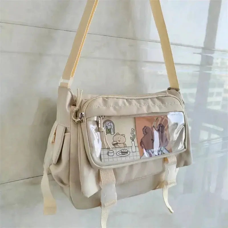 Canvas crossbody bag in beige with large capacity, adjustable strap, and a clear front vinyl pocket with cartoon art.