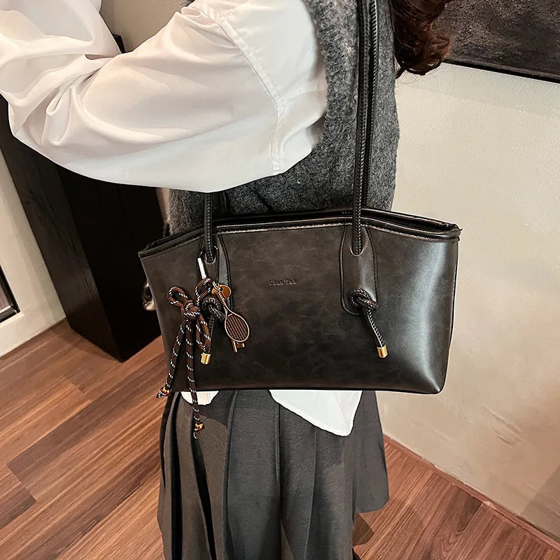 PU leather shoulder bag for women, black with dual top handles and a rope tassel charm.