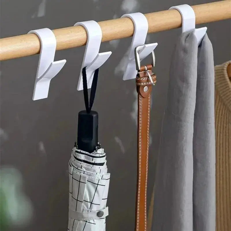 White bathroom towel hooks on a wooden rod holding three items: belt, umbrella, and scarf.