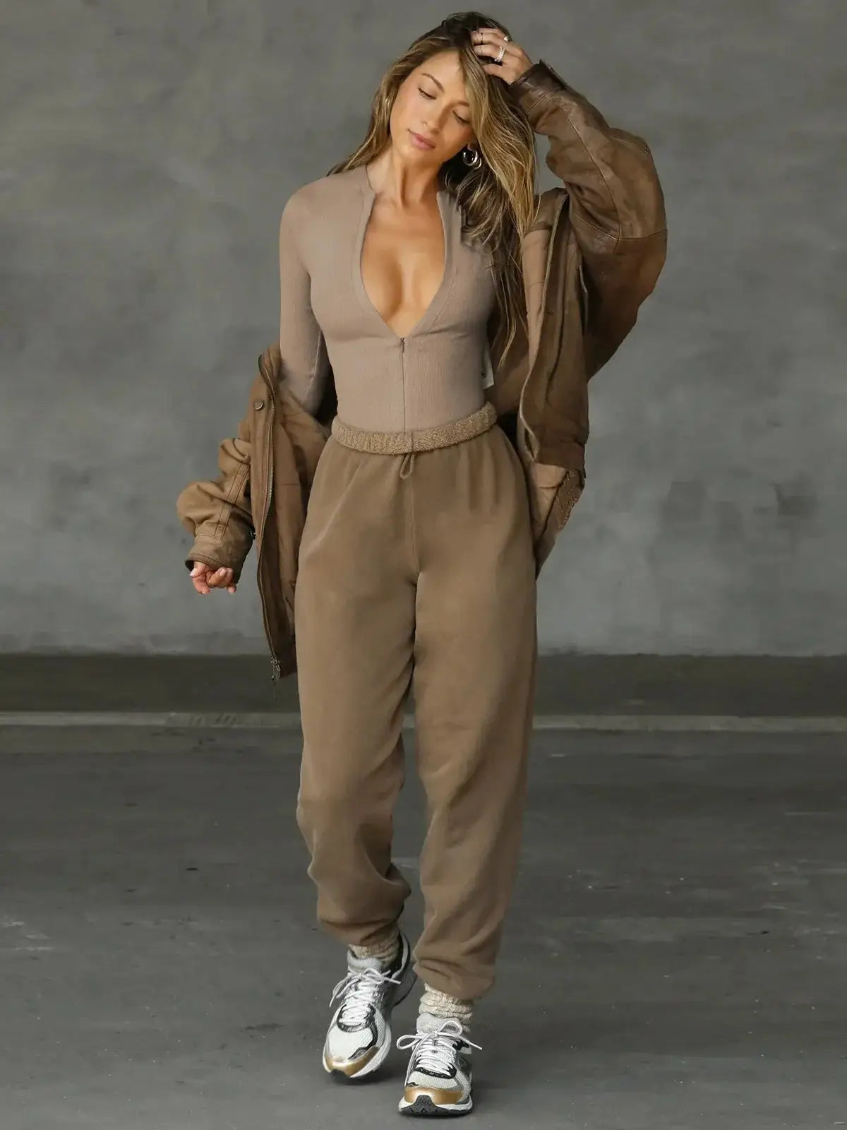 Women's taupe knit jumpsuit with zipper top; 3-piece look paired with brown bomber jacket and sneakers.