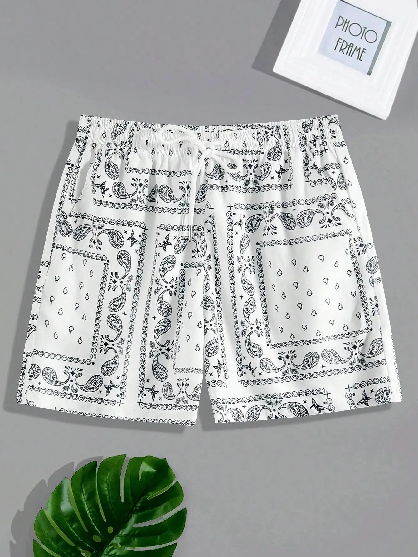 Men's bandana-print beach shorts in white with black paisley patterns, drawstring waist.