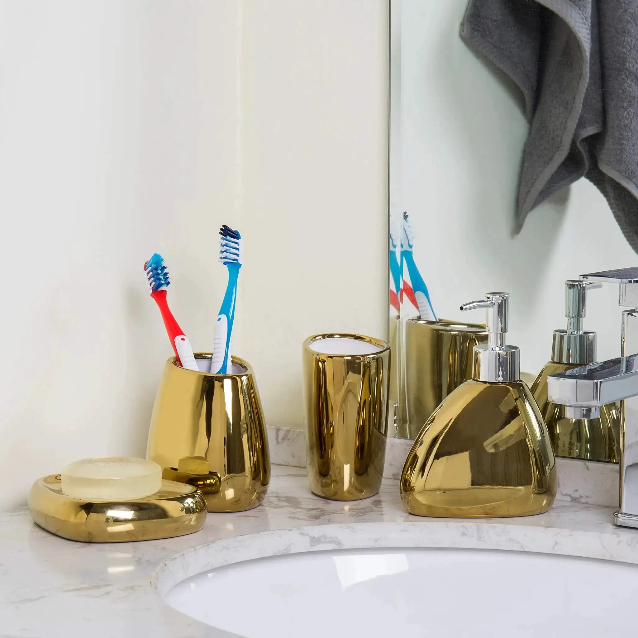 Gold-tone metal 4-piece bathroom accessory set with soap dispenser, mouthwash cup, toothbrush holder.