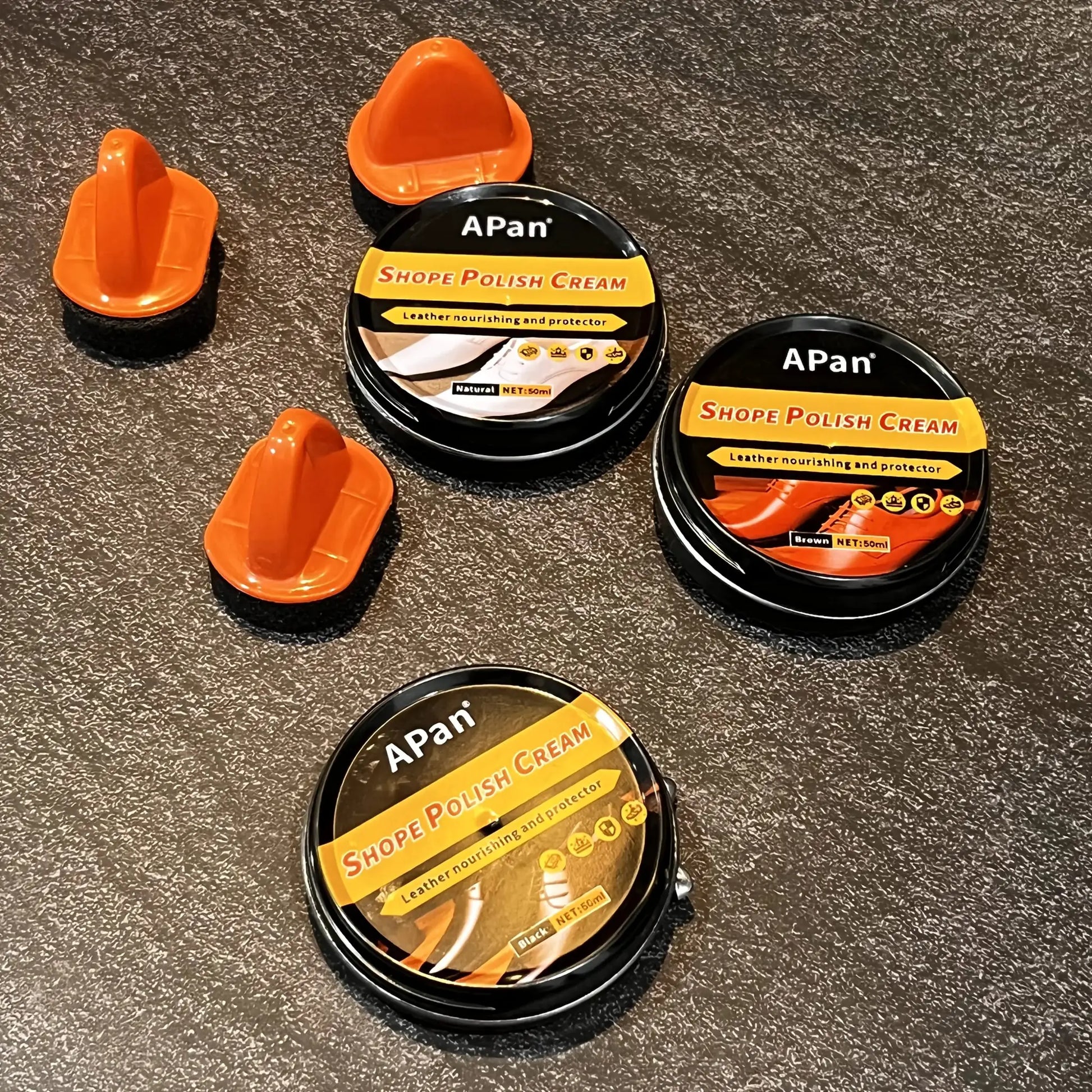 APan shoe polish cream tins with orange caps on a dark speckled surface