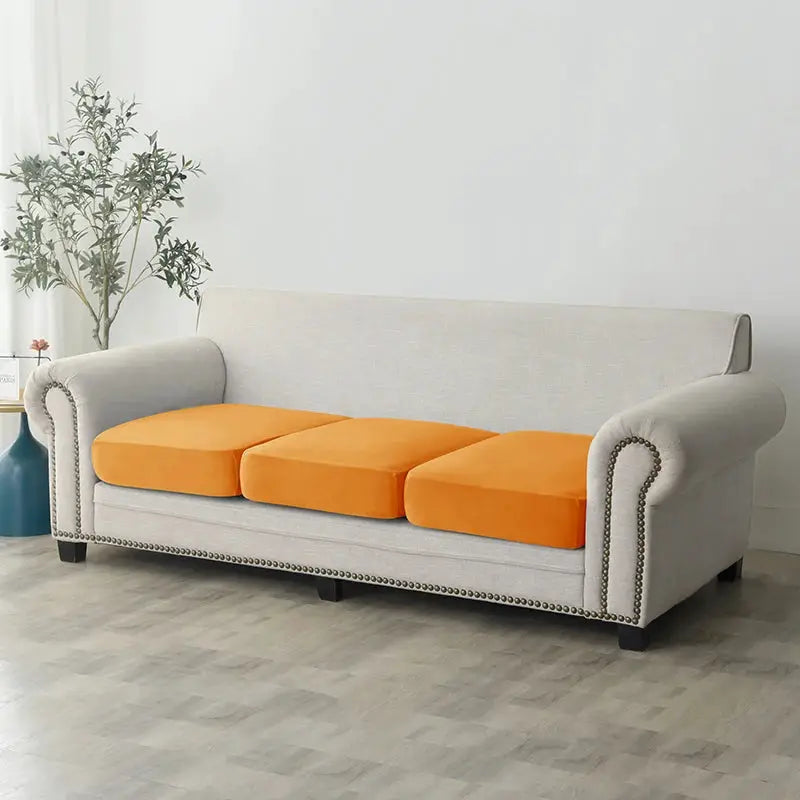 Sofa slipcover in beige with three orange cushions on a living room sofa.