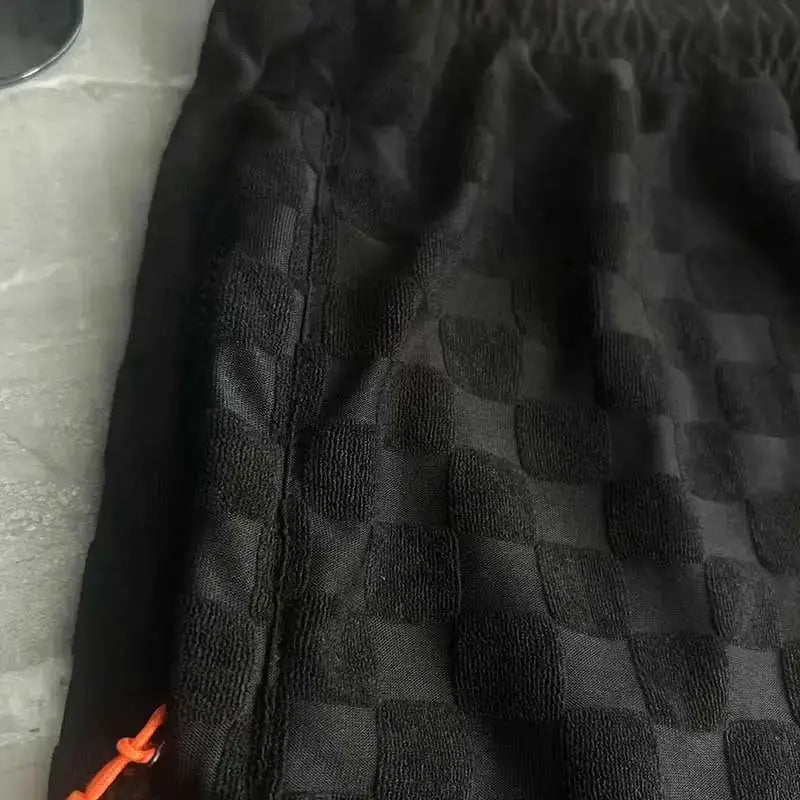 Men's black checkerboard shorts with orange drawstring and zipper pocket