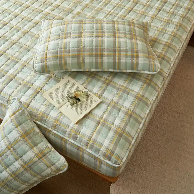 Quilted plaid mattress protector in pale mint with yellow accents on bed with a matching pillow.