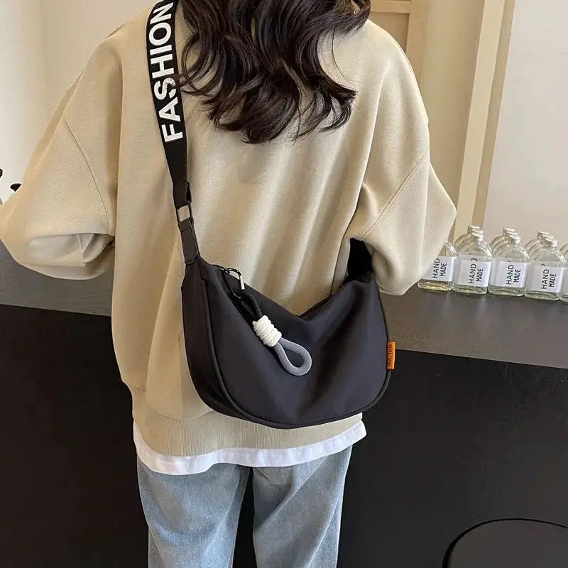 Crossbody bag in black with a wide strap and white rope detail, worn by a woman in a beige sweater.