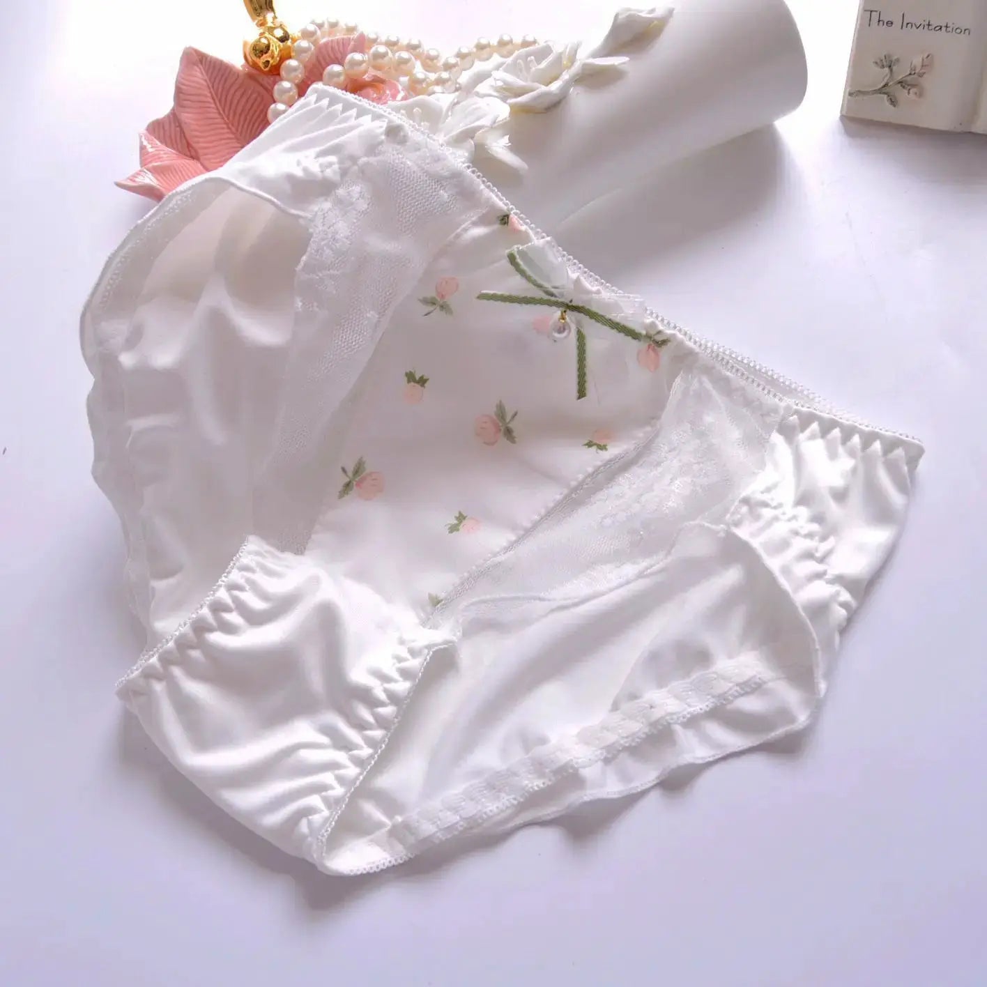 White floral-print panties with lace trim and small green bow accents on soft white background