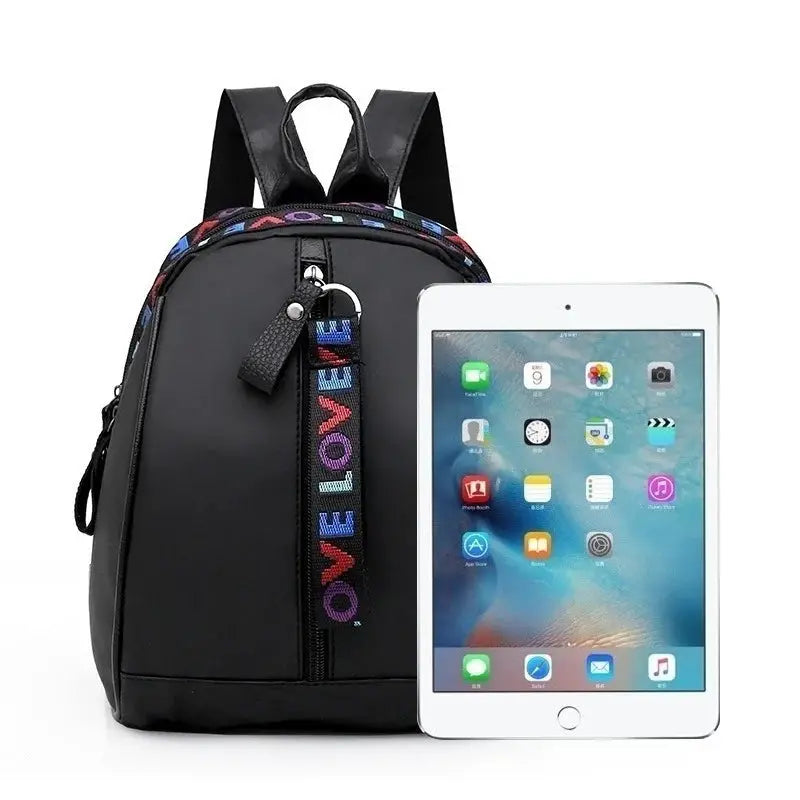 Mini black canvas backpack for men with front vertical zipper and colorful LOVE strap, shown beside tablet.