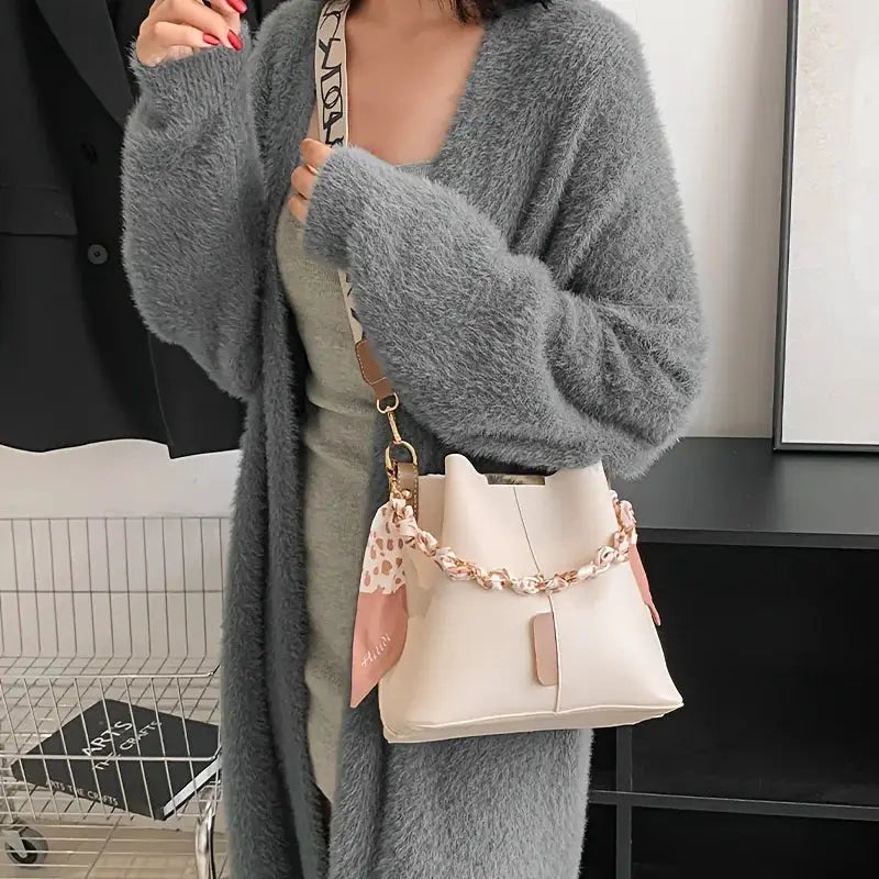 Bucket bag in cream with pink scarf accent, worn crossbody by a woman in a fuzzy gray cardigan.