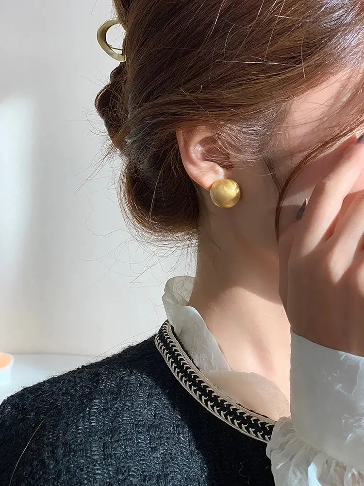 Gold-tone brushed metal stud earring worn by a woman.
