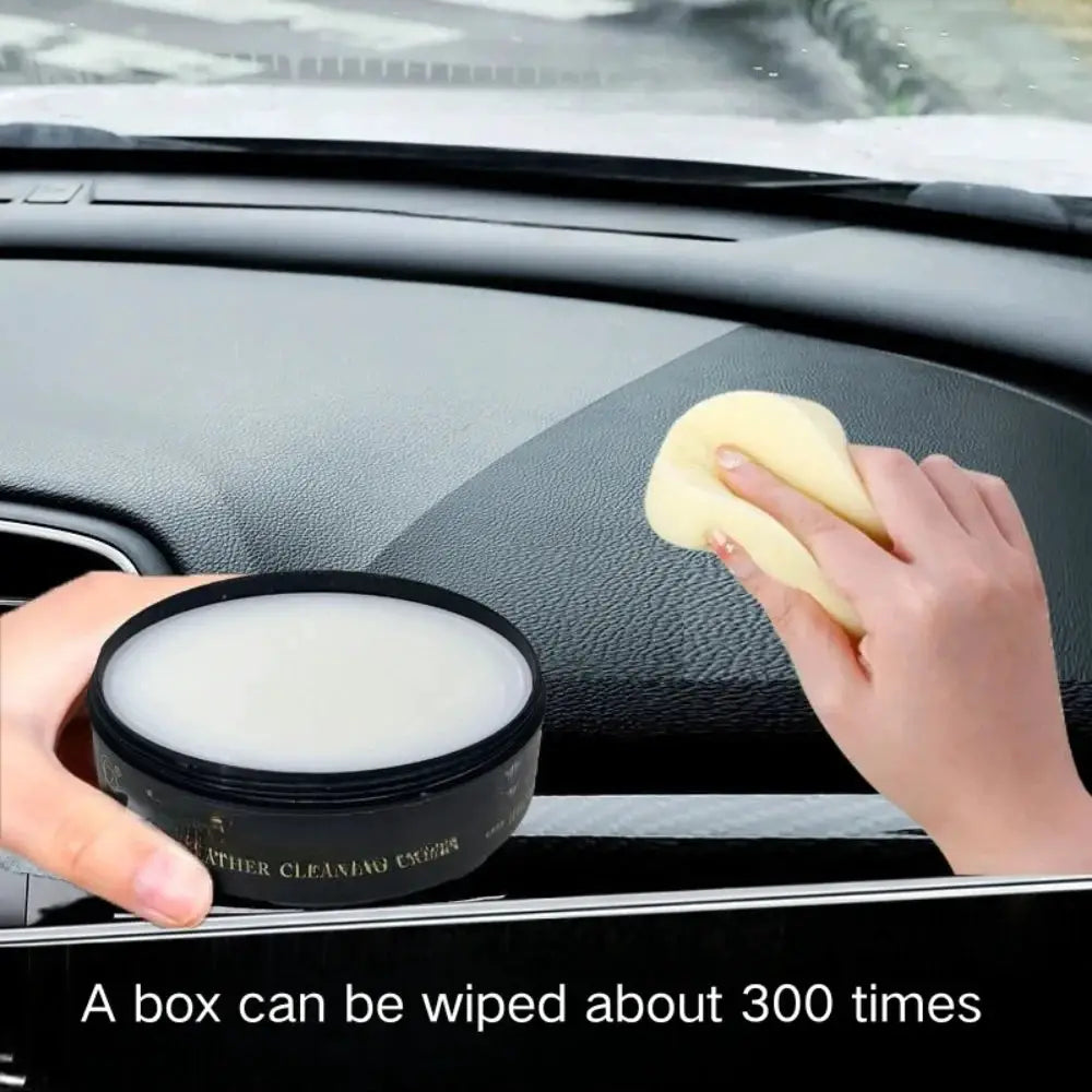 Leather cleaning cream in a black jar with white cream, being applied to a car dashboard with a yellow sponge.