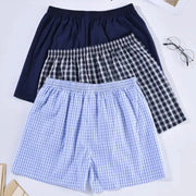 Three men's cotton boxers shorts in navy solid, black-and-white plaid, and light blue gingham with elastic waistbands.