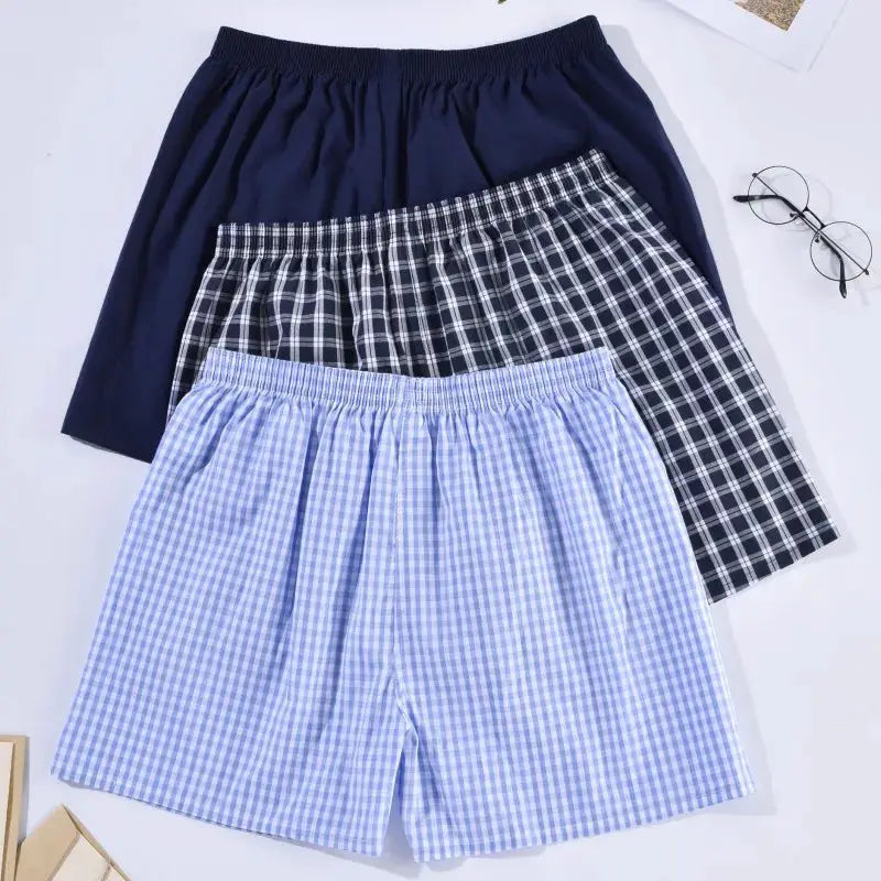 Three men's cotton boxers shorts in navy solid, black-and-white plaid, and light blue gingham with elastic waistbands.