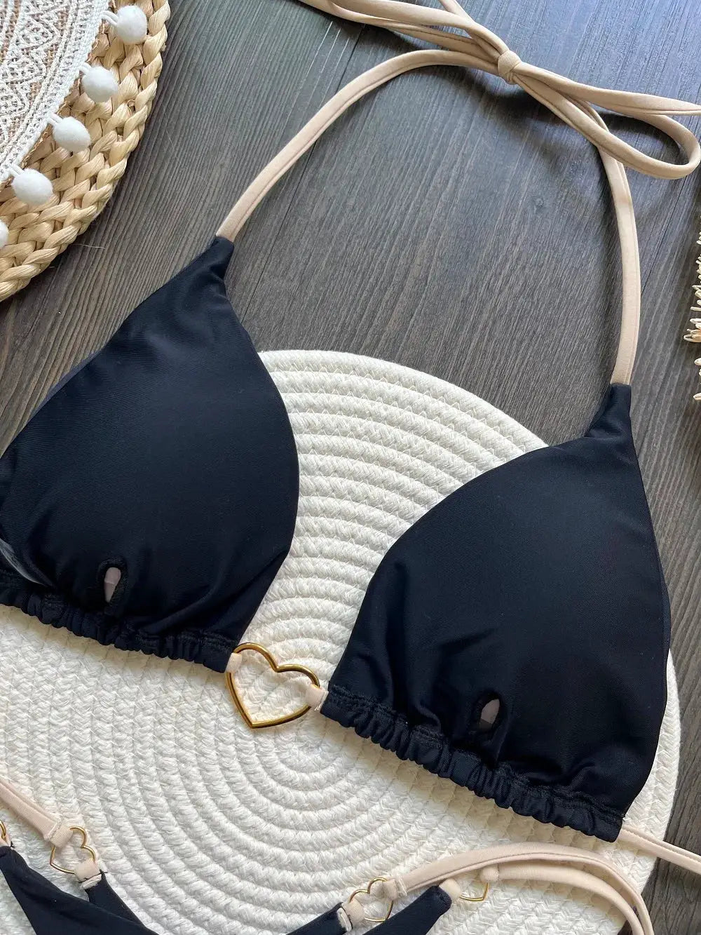 Two-piece black bikini set with triangle halter top, beige straps, and a gold heart ring; matching bottoms.