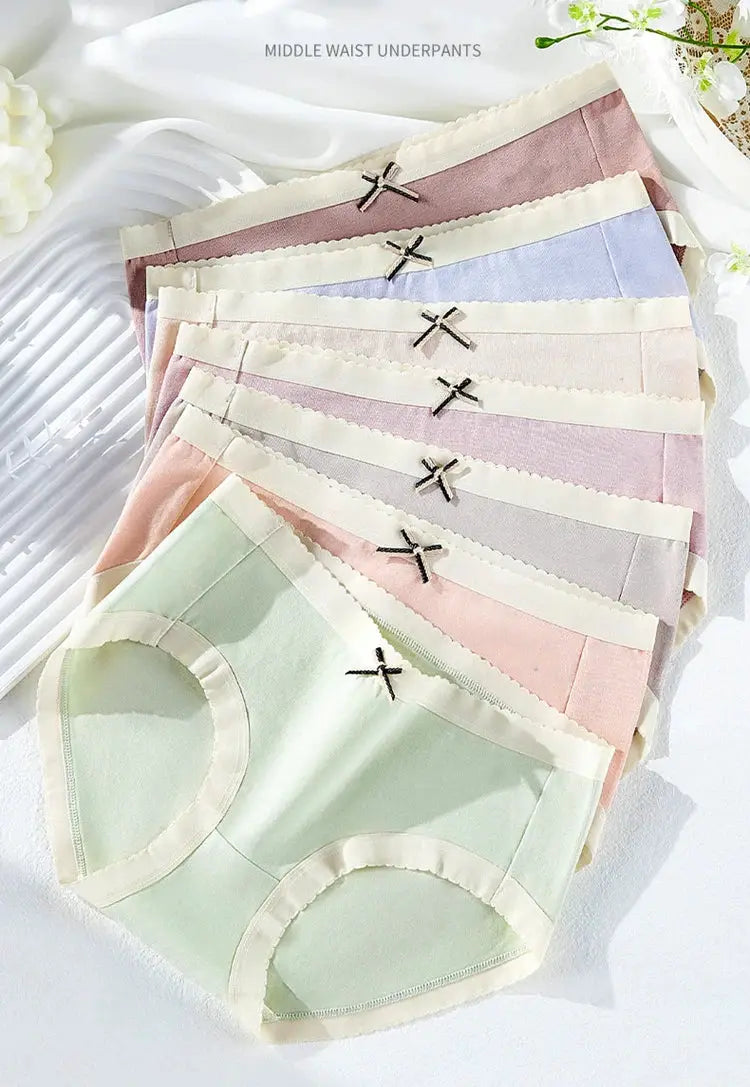 7-pack women's cotton panties in pastel solid colors with cream scalloped trim and small black bows.