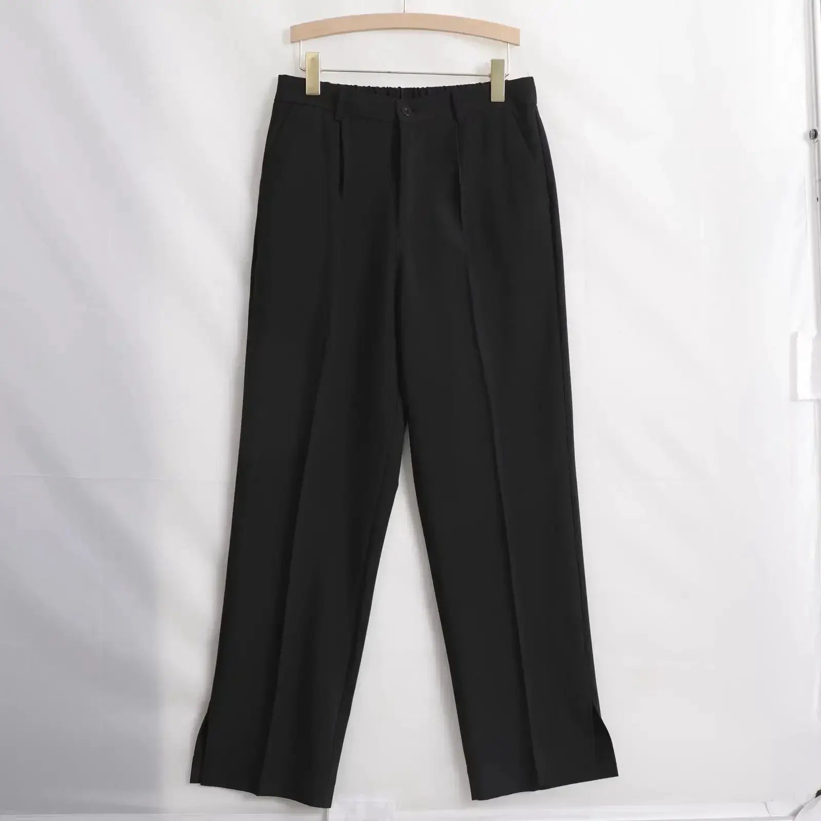 Black men's straight baggy casual pants with front pleats, hanging on a wooden hanger