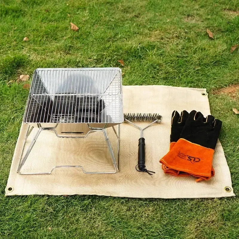 Fireproof fiberglass camping mat with portable grill, cleaning brush, and black/orange gloves on grass.