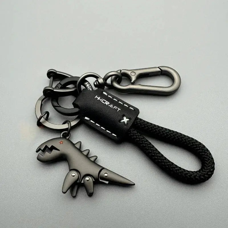 Keychain with gray dinosaur charm, braided black rope, black leather tag, and metal clip