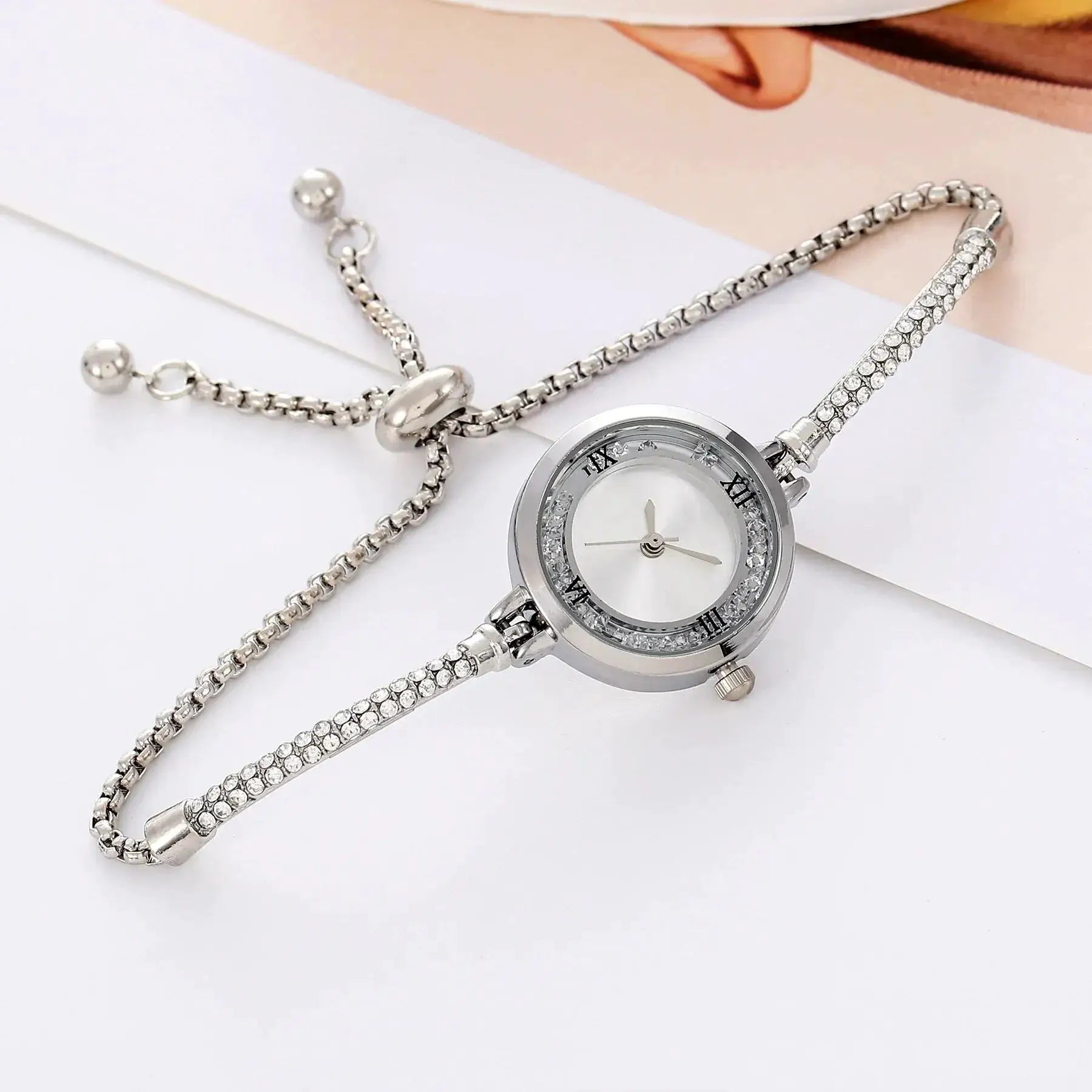 Silver women's wristwatch with crystal-studded bracelet, round dial with Roman numerals.