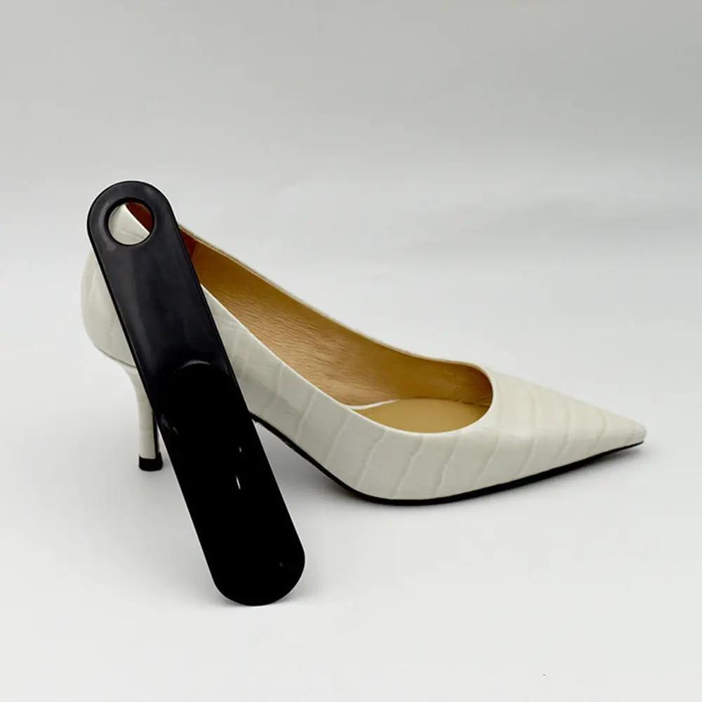 Shoe horn and white pump, black plastic spoon-shaped lifter leaning against a white pointed-toe shoe.