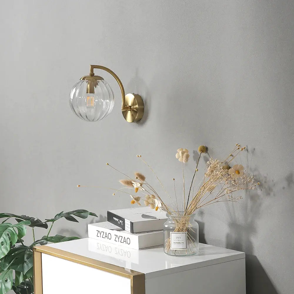 Modern LED wall lamp with clear glass globe shade and brass curved arm, gold finish