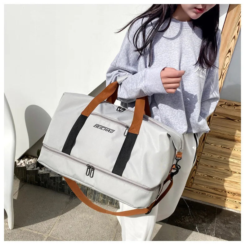 Large gray travel gym bag with brown handles and black vertical straps carried by a person in a gray hoodie.