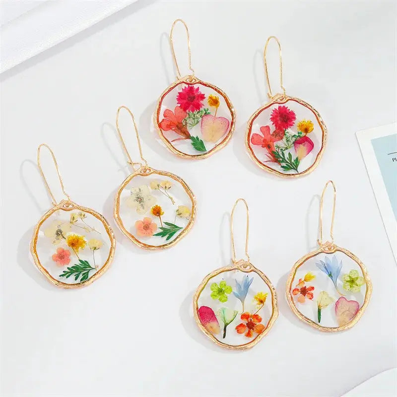 Six round pressed flower resin earrings with gold-tone frames and hooks, colorful blooms